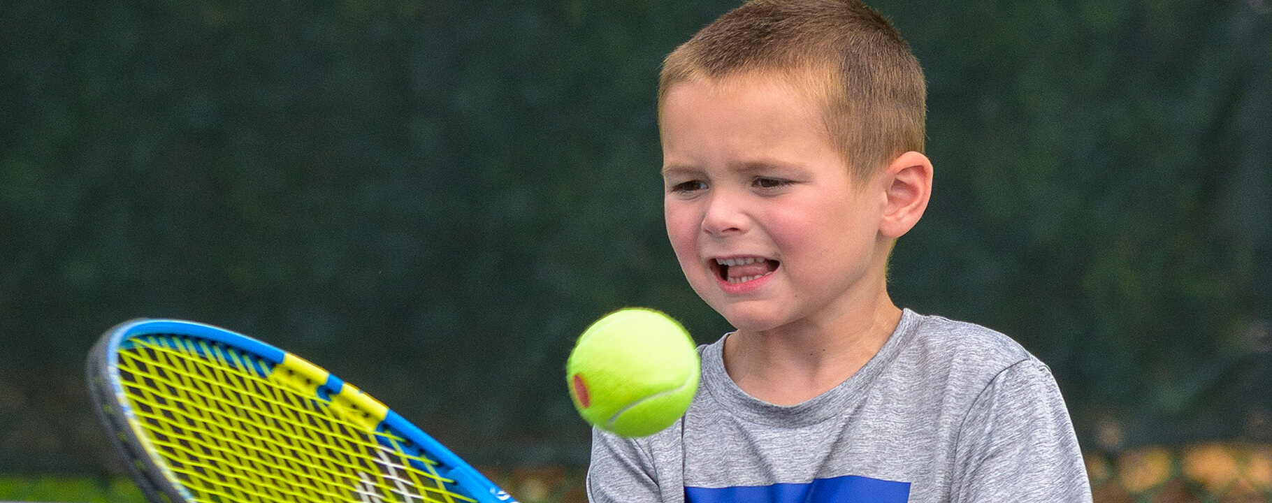 young boy hitting tennis ball with racquet